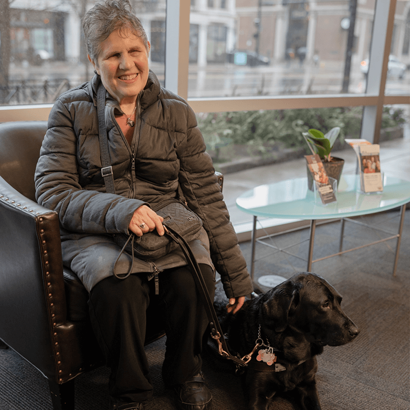 Blind older adult sits smiling with her service dog